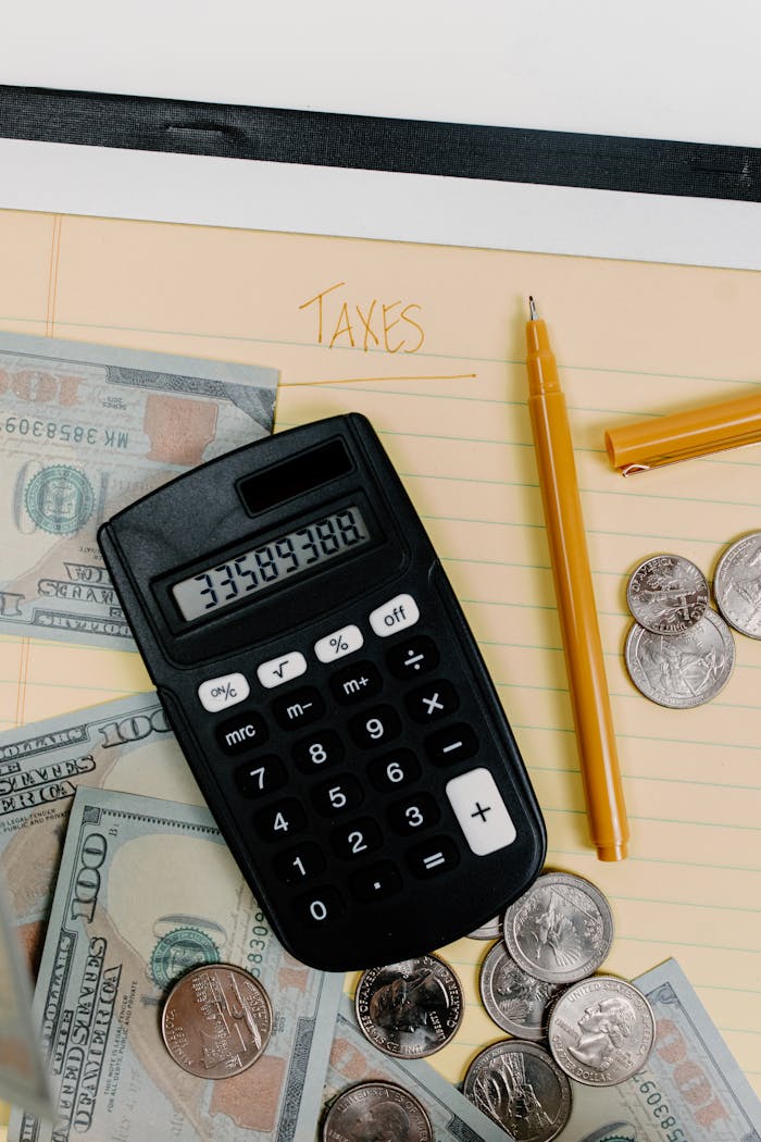 A financial planning setup with calculator, cash, and coins on a notepad labeled Taxes.